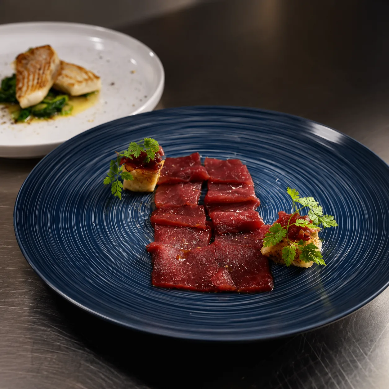 Beef carpaccio with herbs on blue plate
