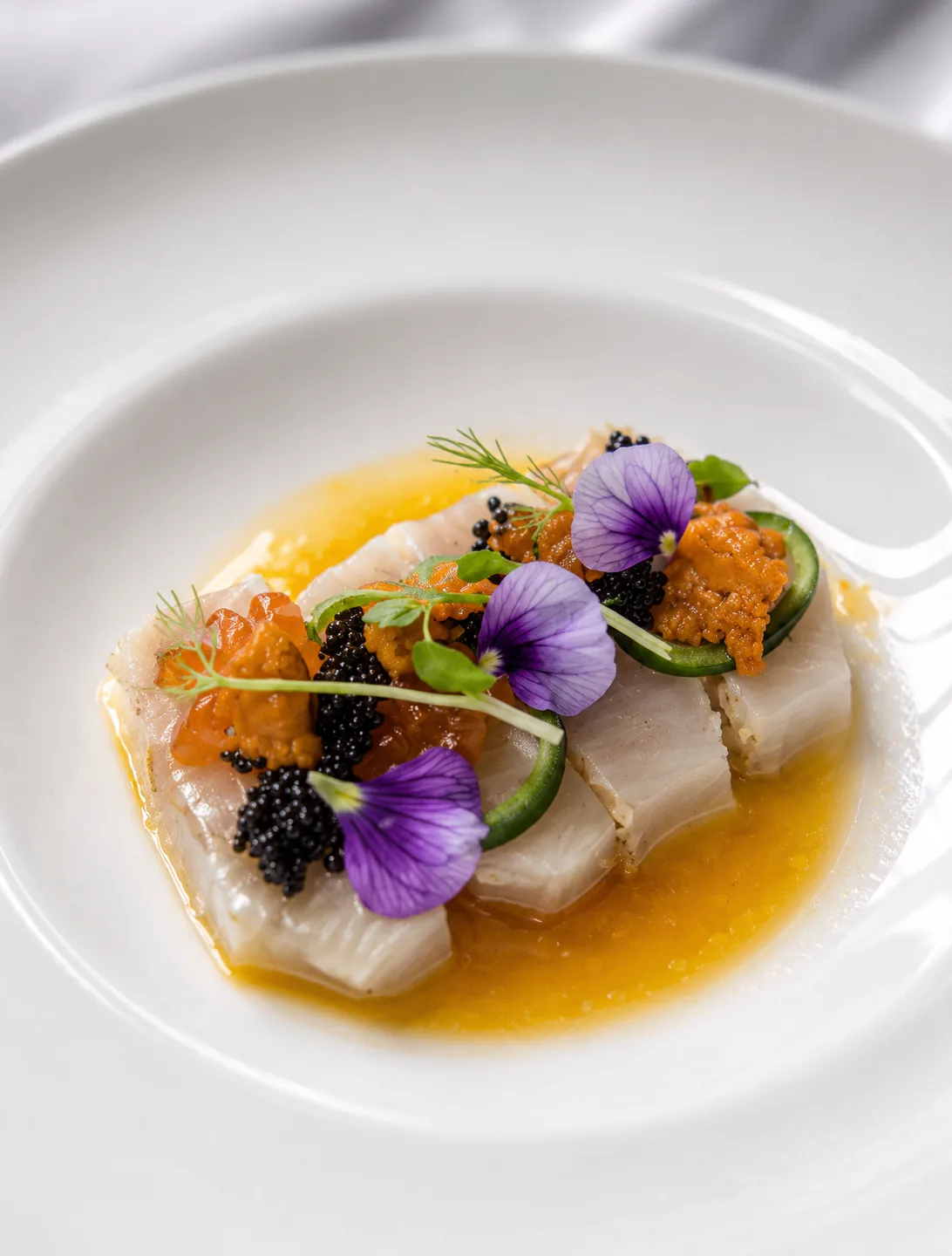 White fish crudo with sea urchin, caviar, and purple flowers